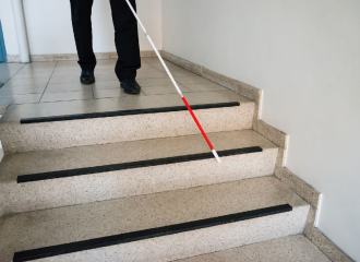A blind man is using a long white cane and approaches some steps