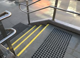 Yellow stair tread nosing strips on wet concrete, with black discrete tactile indicators on both stair landings